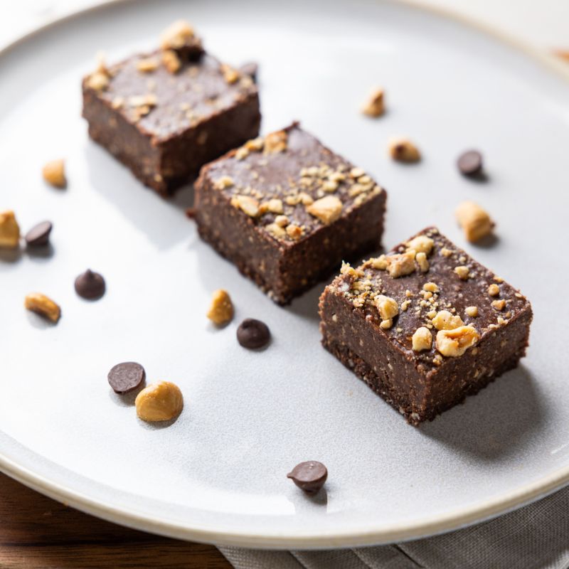 A close-up photograph of three "Nutessa" chocolate hazelnut slices in a row on a white plate. The plate also contains chopped hazelnuts and chocolate chips.