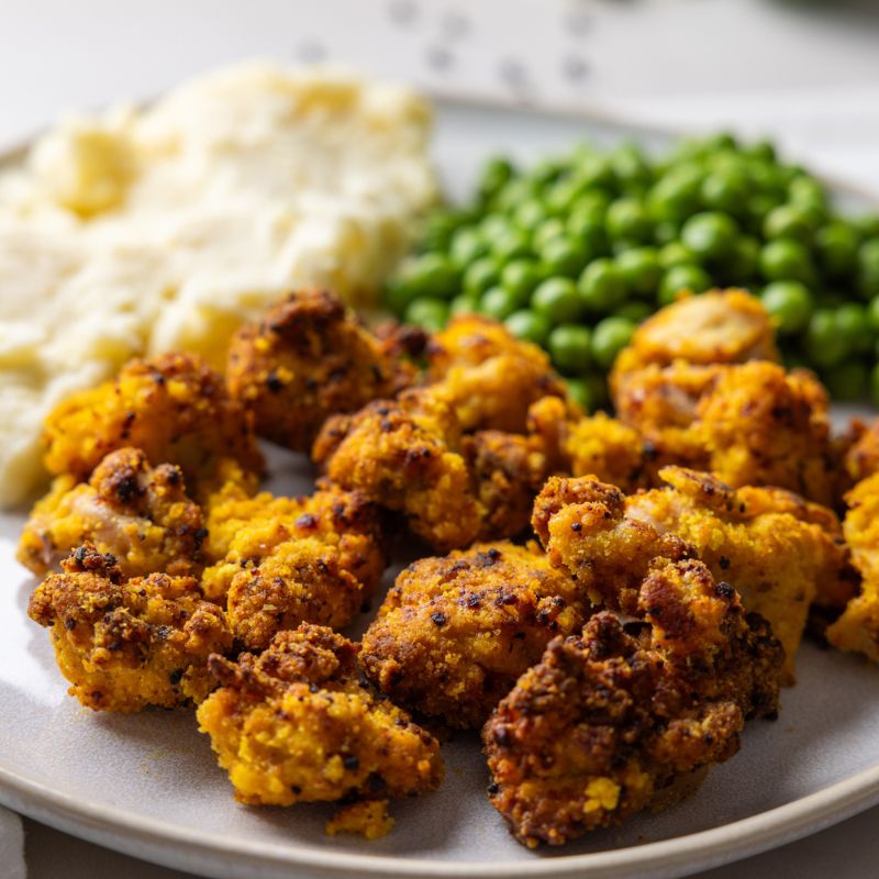 A close-up shot of Popcorn Chicken with Mash, highlighting the crispy golden popcorn chicken, creamy mashed potatoes, and bright green sweet peas. The textures of the dish—crispy chicken and velvety mash—are emphasized.