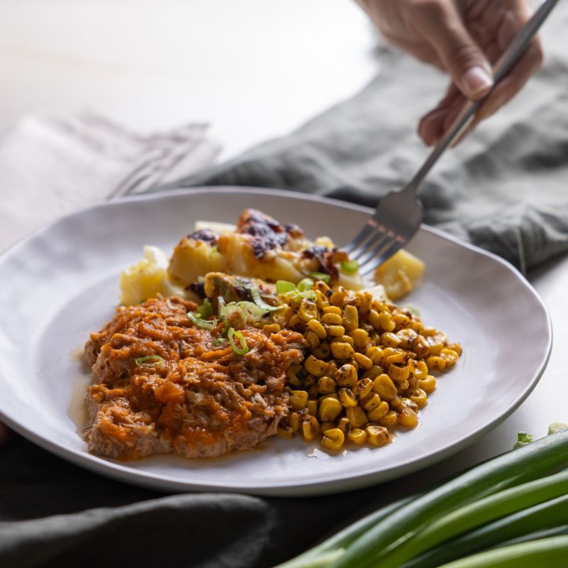 Action shot of a fork digging into the BBQ Pork Shoulder with Delmonico Potato on the plate, emphasizing the tender texture of the pork and creamy potatoes