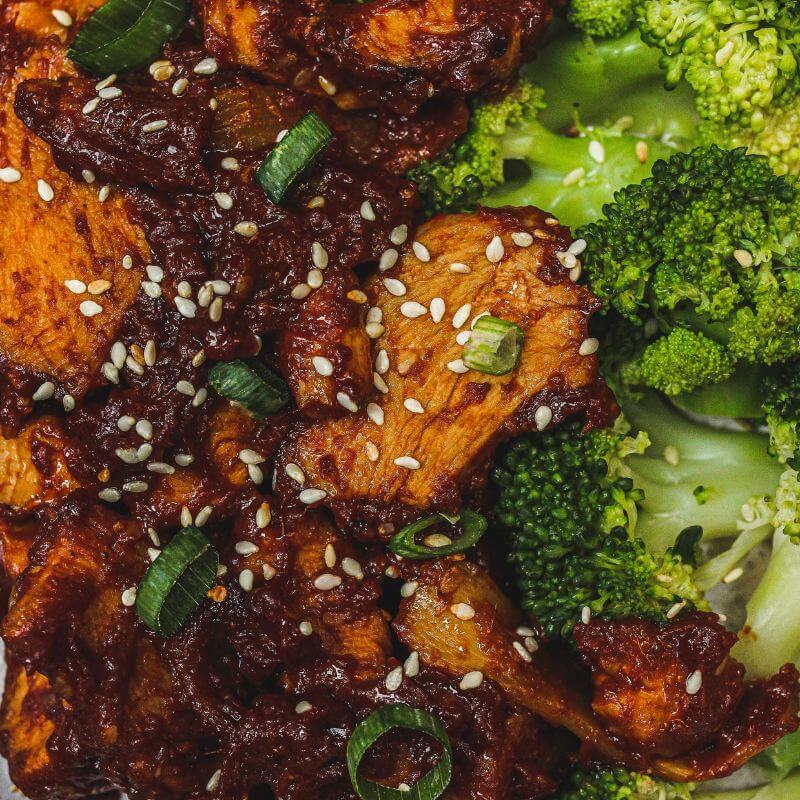 Close-up shot of Korean Sesame Chicken and Broccoli, focusing on the juicy chicken coated in sticky sesame sauce, topped with sesame seeds, and perfectly steamed broccoli.