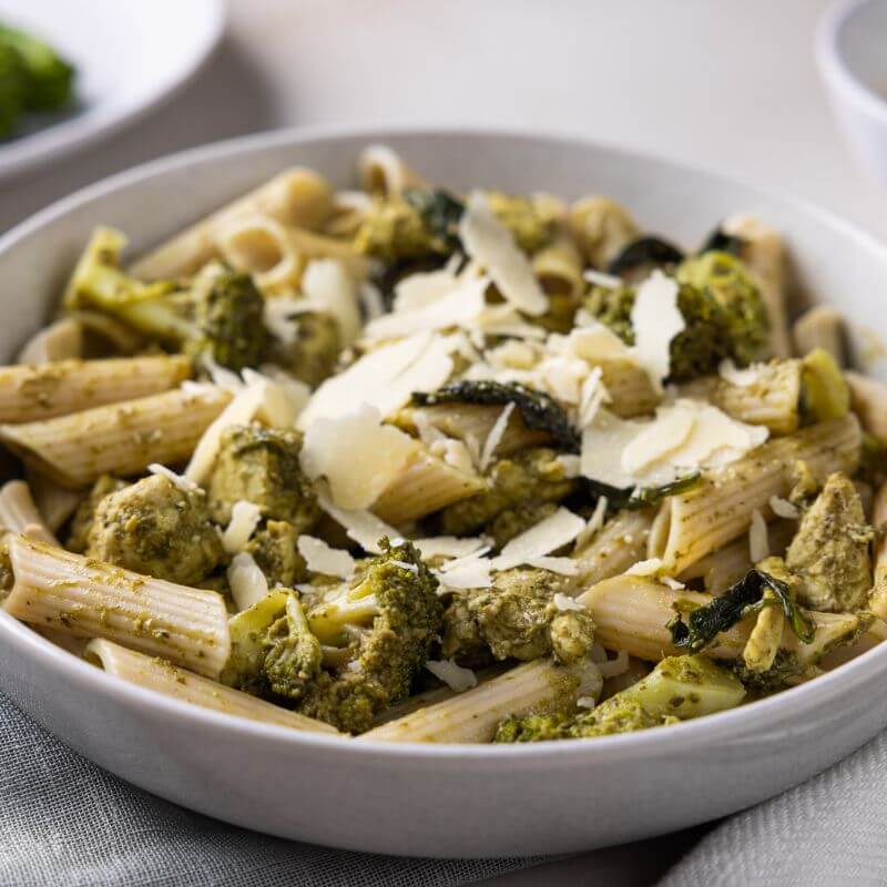 Close-up shot of Chicken Pesto Penne in a white bowl, highlighting the vibrant pesto sauce, gluten-free penne pasta, and tender pieces of chicken breast.