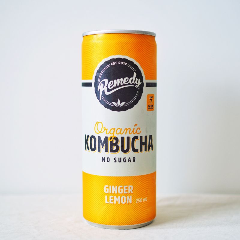 A yellow 250ml Remedy Kombucha can, sitting on a marble bench with a white back drop. 