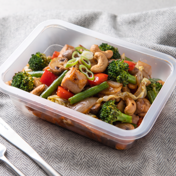 Packaged ready-to-eat Chicken Cashew Stir Fry meal presented inside a meal-prep container with fresh vegetables and roasted cashews.