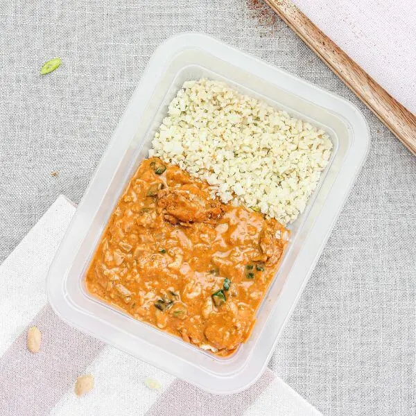Clear container shot of the Kung Pao Chicken, neatly presented with the fried cauliflower rice and garnished with spring onion. The container sits on the light grey cloth for a clean and inviting presentation.