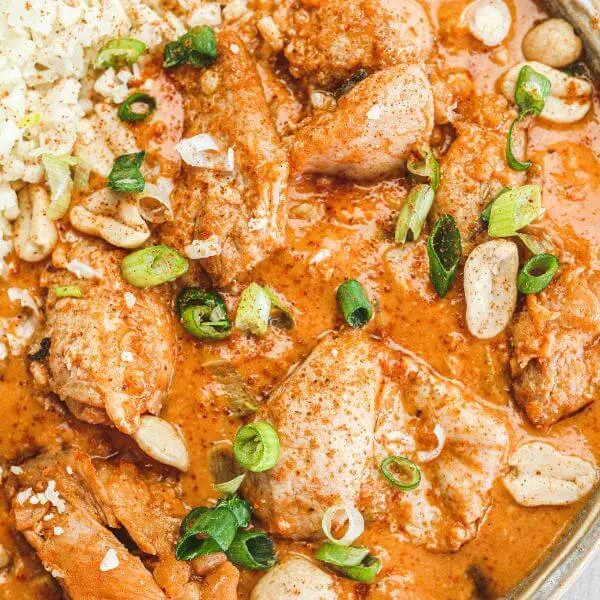 Close-up shot showcasing the Kung Pao Chicken in detail. The glistening sauce, tender chicken thigh pieces, and fresh garnish of spring onion take center stage, with a soft focus on the background elements for added depth
